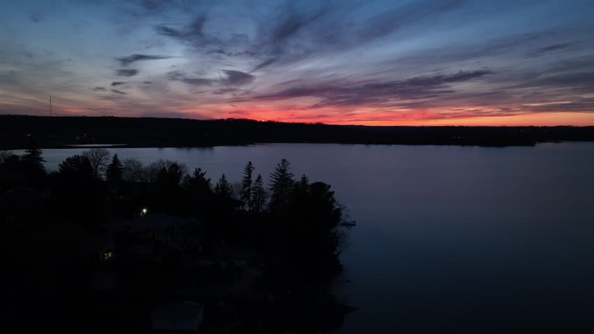 An aerial scenic view of a lake with silhouette of trees under colorful sunset sky
