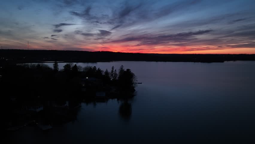 An Aerial scenic view of a lake with a silhouette of trees under colorful sunset sky