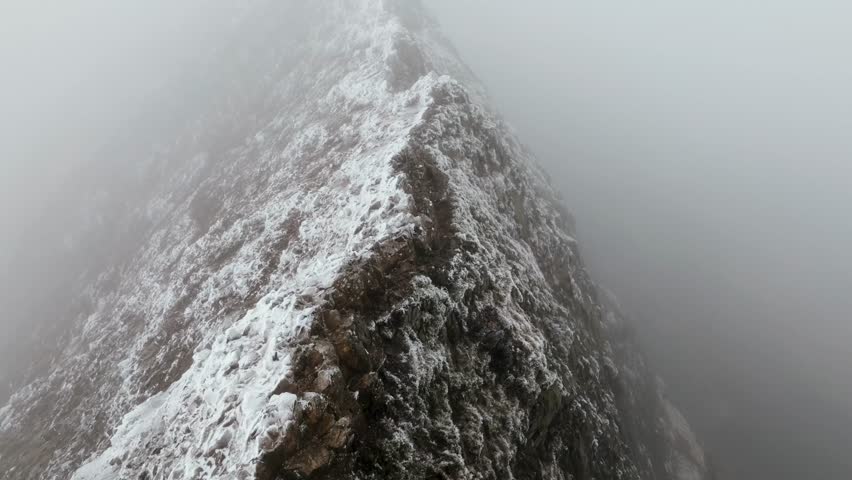 A Drone footage of Snowdonia Rugged Peak with snow covered rocks behind fog