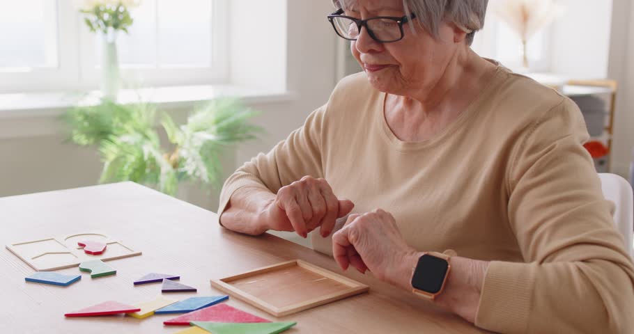 Senior woman enjoys leisure at home, playing board game or solving puzzle for entertainment, focusing on fun in a personal setting with engagement and relaxation during the activity.