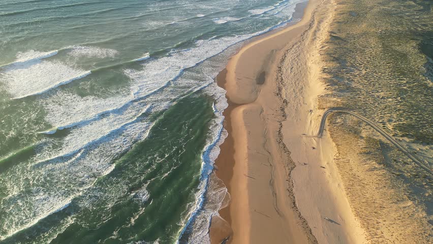 An Aerial view of Atlantic coastline featuring sandy beach and ocean waves at the golden hour in Cap Ferret, Nouvelle-Aquitaine, France