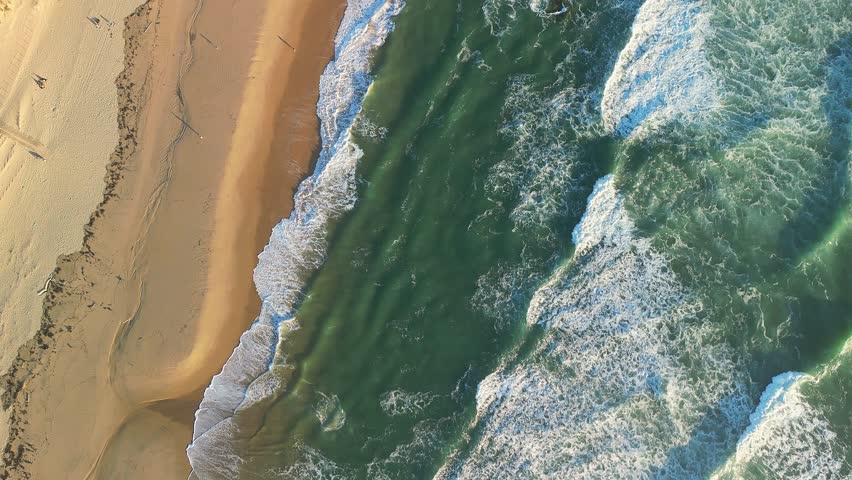 An Aerial view of Atlantic coastline featuring sandy beach, ocean waves, and a partially sunken World War II German bunker in Cap Ferret, France
