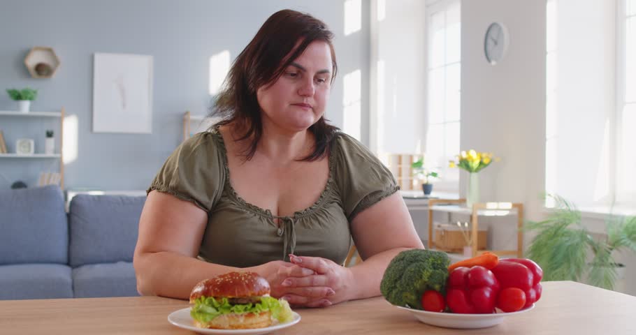 Tempting food, diet break, obese hungry woman with excessive fat choosing to eat unhealthy fast food, tasty hamburger, juicy burger, cheeseburger, chubby overweight plus size big fat, excess calories 