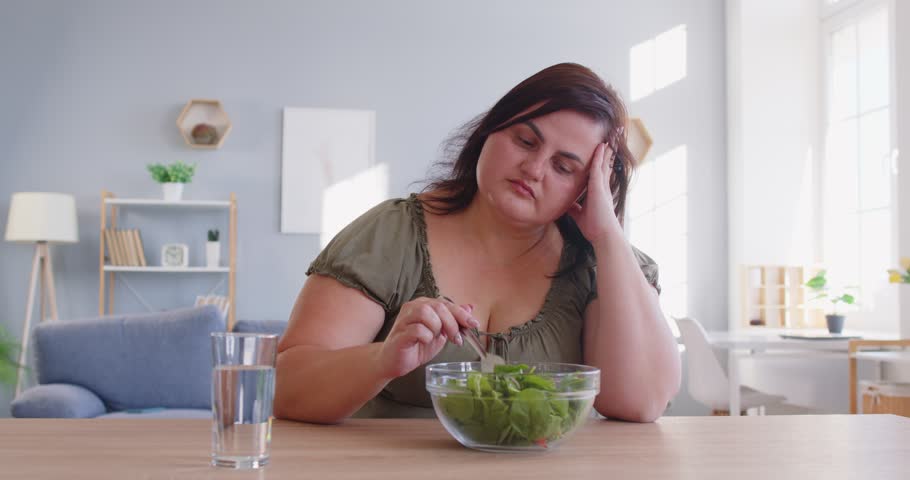 Bored of eating green vegetables, veggies diet for dinner, pleasant obese woman sitting at home, chubby overweight plus size big fat fit lady sad with no progress in weight loss looking in despair 