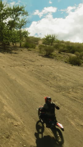 Motorbiker rides vehicle up bushy hill fpv drone. Strong skilled racer in helmet drives to mountain peak at extreme racing. Motocross at highland