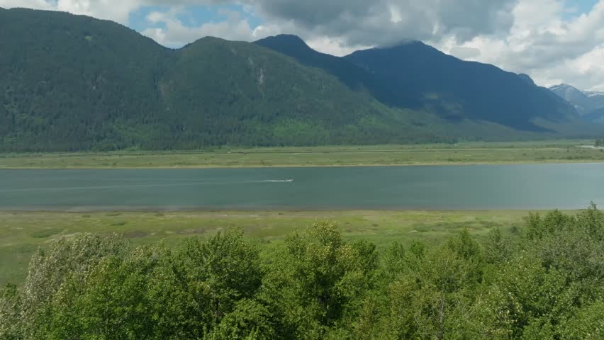 A peaceful drone view of a tranquil lake nestled in lush greenery, with a boat gliding gently across and mountains rising in the distance