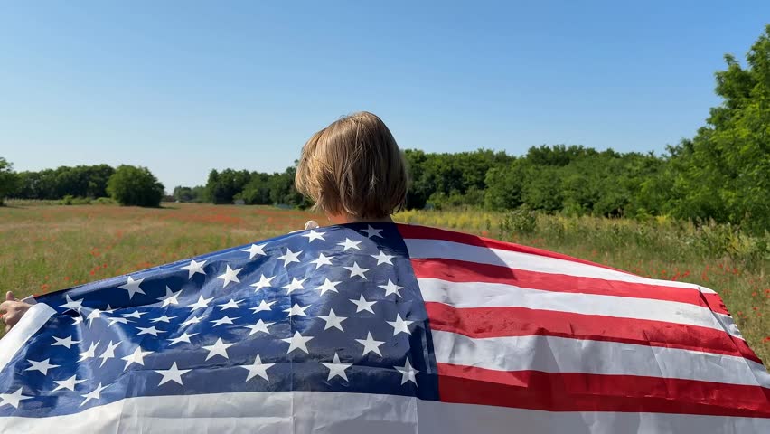 A young Caucasian boy draped in an American flag stands in a rural field, symbolizing patriotism, freedom, and Independence Day Americana vibe