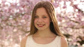 Smiling girl looking at camera during spring time under cherry blossom trees