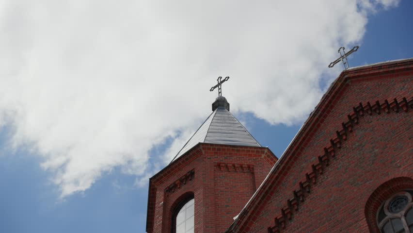 The red brick steeple and cross of Saciai St. John the Baptist Church in Sates, Lithuania under cloudy skies