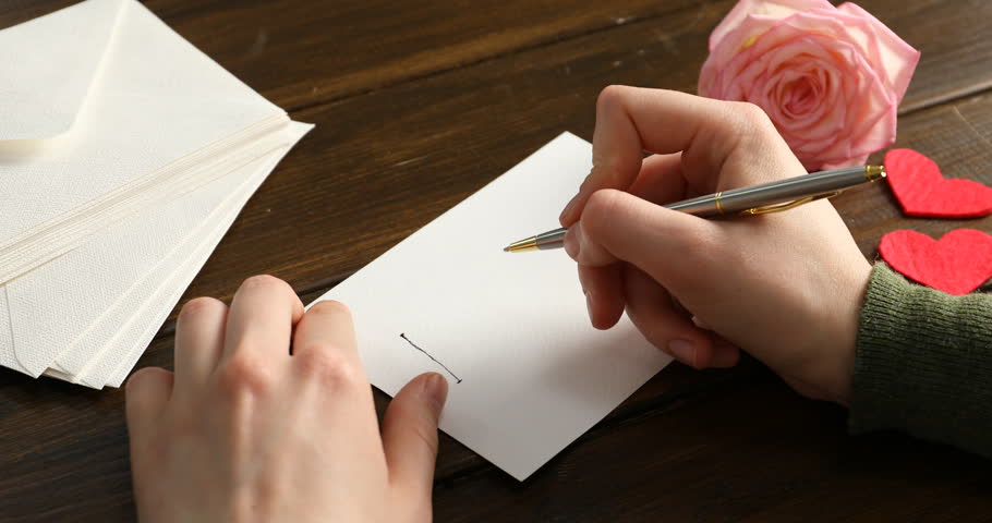Woman writing phrase I Love You on card at wooden table, closeup