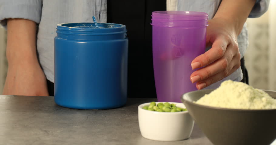 Woman adding protein powder into shaker and green peas at grey table indoors, closeup