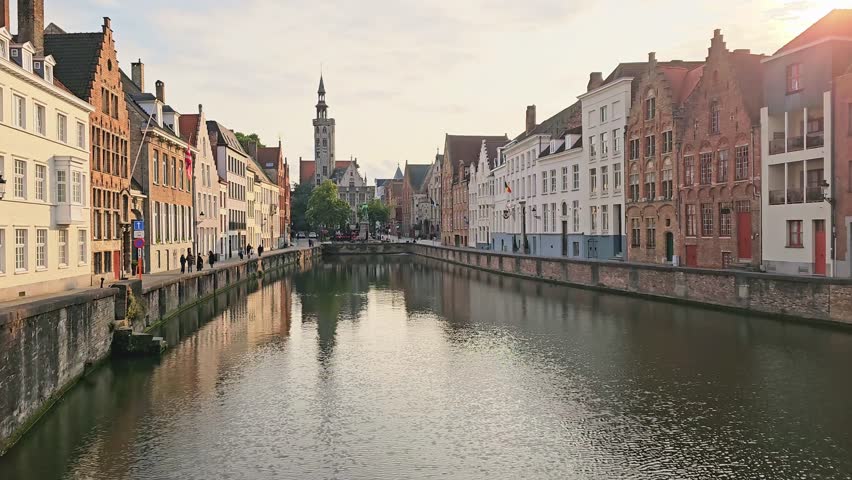 Medieval buildings lining the picturesque canals of Bruges, Belgium at sunset. Slow handheld upward panning motion.