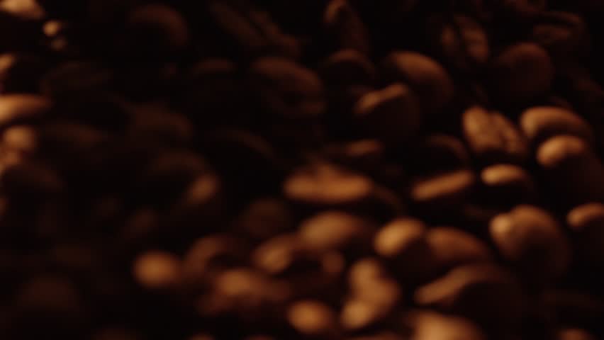 Warm light illuminates roasted coffee beans, some are poured from a wooden scoop and stirred, creating a captivating scene of coffee production