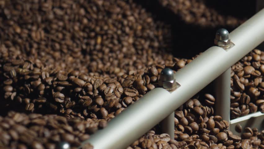Roasted coffee beans are mixed by a rotating arm inside an industrial roasting machine, ensuring even heat distribution during the roasting process in a workshop