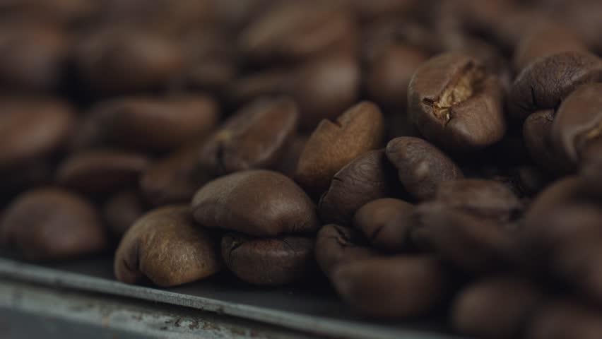 Freshly roasted coffee beans resting on textured surface, gently shifting with soft focus revealing rich, dark texture and aromatic details of premium coffee crop