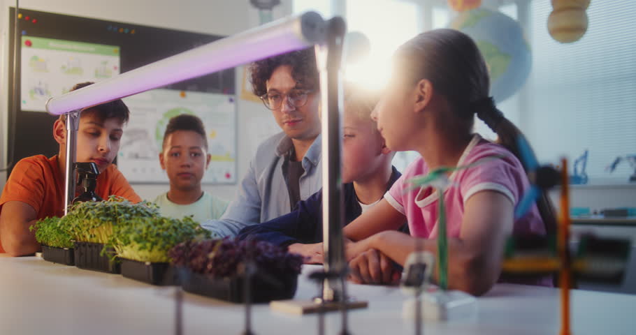 Elementary School Students Sitting at Table, Growing Experimental Microgreens, Studying Biology. Teacher Educating Group of Smart Kids During Science Lesson in Multicultural Classroom. STEM Education.