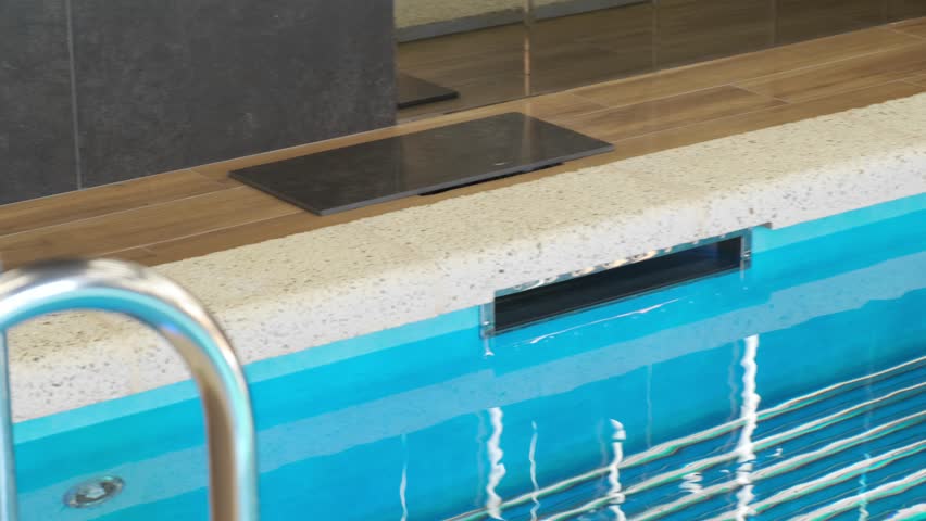 Modern indoor overflow pool with water intake system. Clear blue water, stone finish, and technical details create a cozy, clean, and functional space for relaxation and wellness
