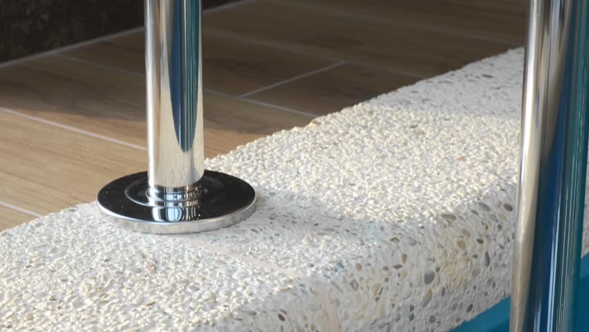 Close-up of a chrome handrail of an indoor overflow pool against dark tiles. Light reflections on metal emphasize the clean and modern design of the spa environment
