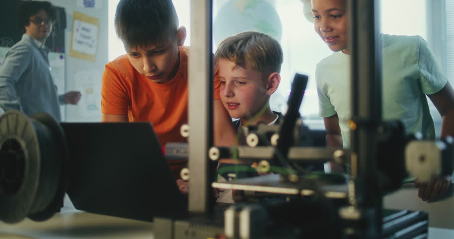 Elementary School Students Writing Code for Advanced Automated 3D Printer on Laptop During Programming Lesson. Smart Young Boys Studying in Group in Multicultural Classroom. Interactive STEM Education
