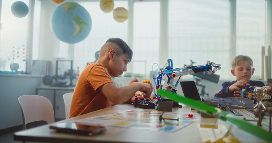 Young Teacher and Kids Doing Team Huddle Gesture in Multiethnic Classroom. Primary School Children Exploring Robotics and Renewable Energy Models, Celebrating Teamwork. STEM Learning. Slow Motion.