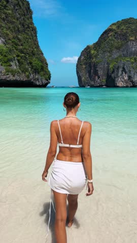 Back view of woman entering turquoise water at Maya Bay, Koh Phi Phi. A concept of luxury vacation, freedom, beauty and tropical travel lifestyle. Ideal for summer promo content.