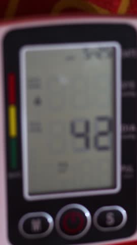 A close-up view of a digital blood pressure monitor displaying systolic, diastolic, and pulse rate readings while measuring a patient's vital signs during a medical checkup.