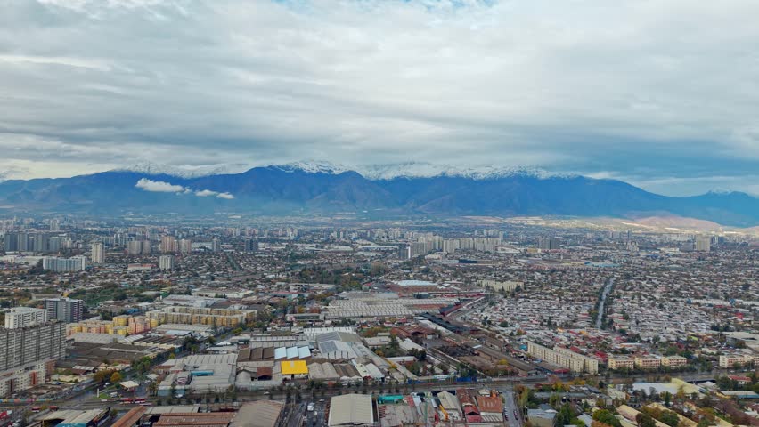 Aerial panoramic fly at Snowed Andean Cordillera mountain range with Santiago de Chile city foothills, daylight