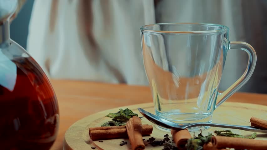 herbal tea being poured into a glass mug with cinnamon sticks and loose leaf tea on a wooden tray. Cozy, warm drink concept with natural ingredients and relaxing atmosphere. Caffeine free herbal drink