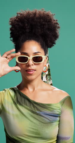 Face, woman and surprise with sunglasses in studio for fashion sale, discount deal or promo offer. Trendy outfit, african person and omg reaction to bargain or retail announcement on green background