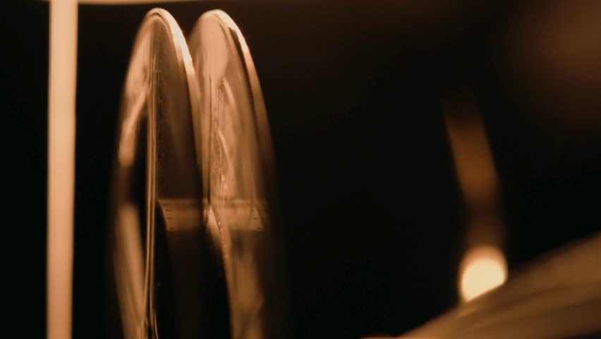 Footage captures vintage film projector, reels spinning quickly, emitting light in dark room, evoking nostalgia and cinematic history. Ideal for creative projects with retro themes.