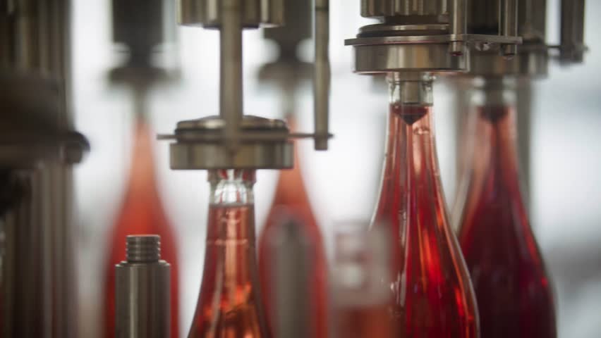 Red wine bottles are sent to the next station of a winery production line after having been automatically filled