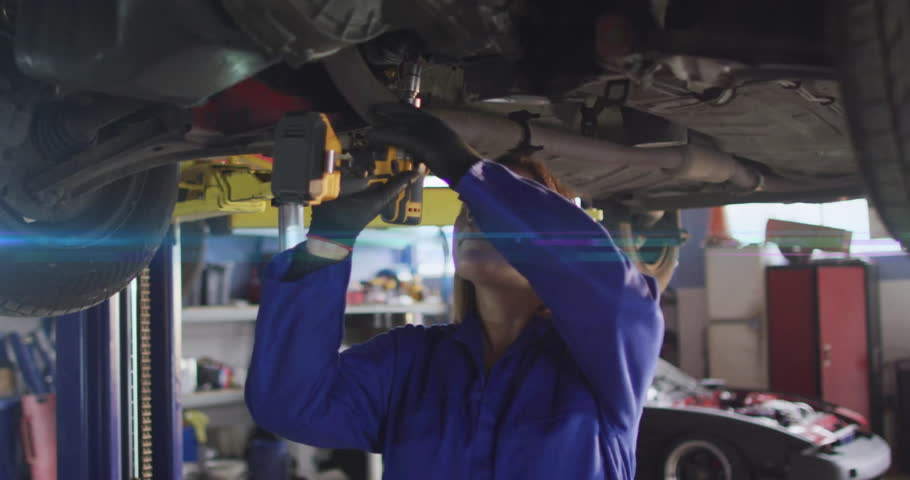 Tech reaching for yellow impact wrench under car, operating tool aligning socket and loosening bolt. Mechanic, industrial, machinery, safety, maintenance, repair, rugged