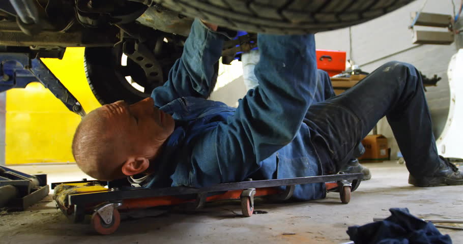 Mechanic gripping wrench under vehicle to loosen bolt and causing filings to scatter in repair shop. Automotive, repair, industry, tools, workspace, craftsmanship, engineering