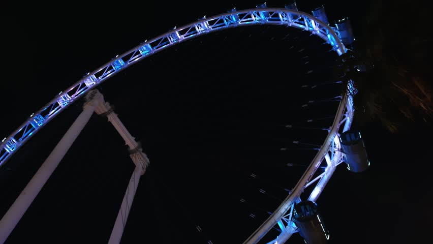 Nighttime Singapore ferris wheel glowing, multicolored cabins rotating slowly against shadowy metropolitan backdrop, highlighting urban architectural landmark