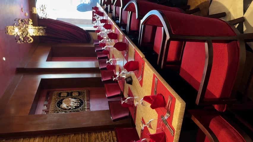 A luxurious, empty dining room with a long table, vibrant red chairs, and ornate wall decorations. Captures elegant Indian restaurant interior design and upscale ambiance