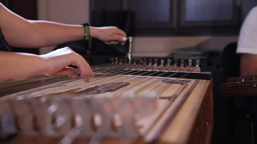 close-up shows a woman's hands playing an ornate wooden zither with plectrums. A microphone captures the beautiful sound of this traditional Middle Eastern folk instrument.