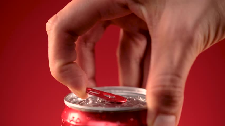 A detailed shot of a wet soda can on a red background, highlighting the refreshing beverage as a person's hand opens it.