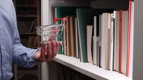 Man holding miniature shopping cart in front of bookshelf, buying books online - Powered by Shutterstock - Get 15% off with code: PIKWIZARD15
