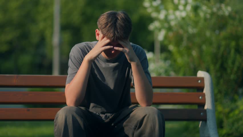 Teenage boy sits alone on a bench with his head in his hands, visibly upset and overwhelmed. A powerful portrayal of stress, emotion, and mental struggle.