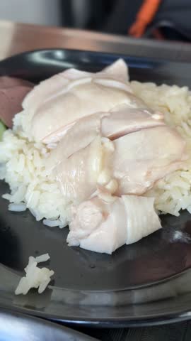 Detailed closeup shot of grilled chicken rice with sauce on black dish served at casual Thai restaurant table