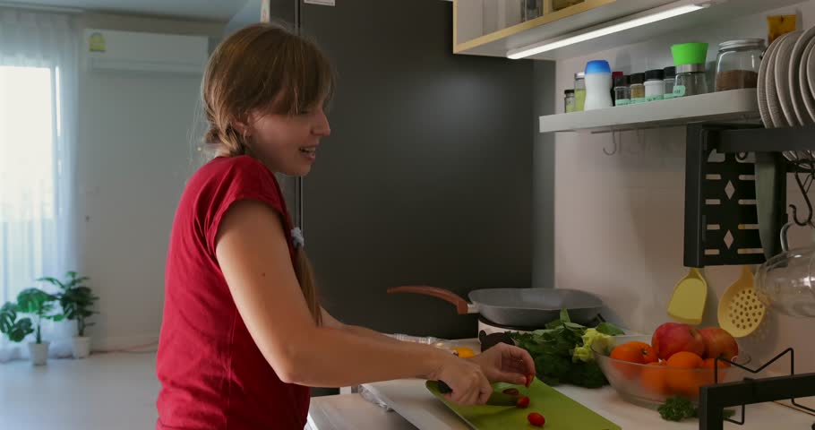 Woman cooking at home with fresh vegetables, dancing and smiling, positive vibe, kitchen fun, social media content creation, home cooking enjoyment.