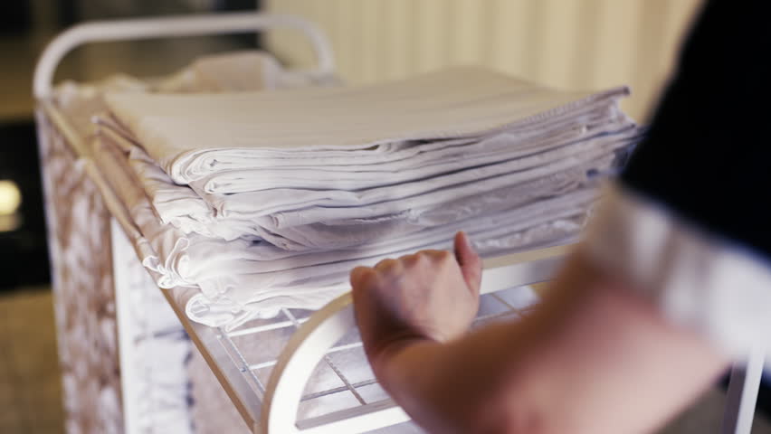 Cleaning staff pushing cart with fresh linen in hotel hallway, room service duty