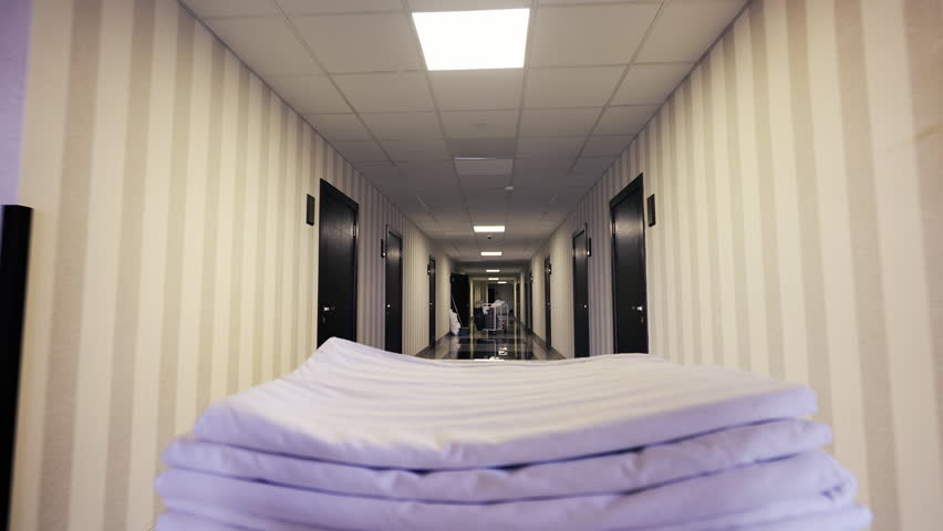 POV of room attendant pushing cart with linen through hotel hallway, cleaning