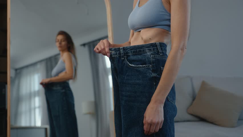 Anorexic slim body woman wearing big jeans standing front of mirror