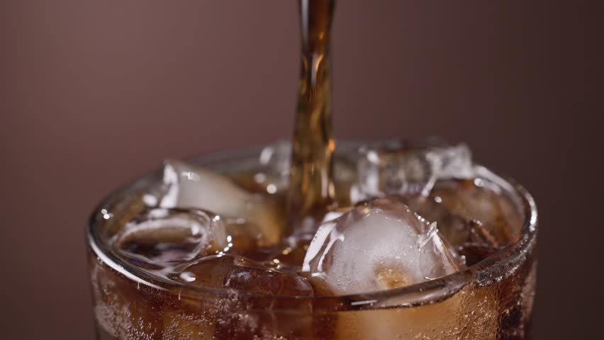 Closeup of pouring cola drink with ice cubes. Fizzing cola with ice in glass. Refreshing tasty cola drink.