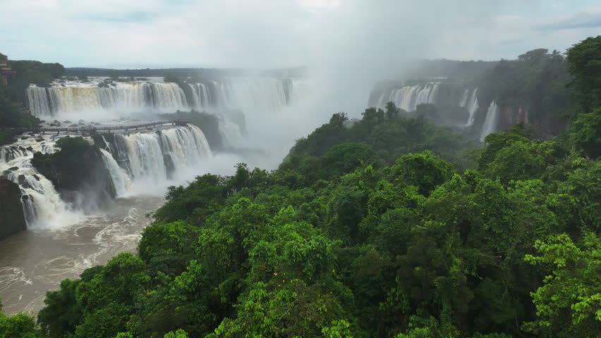 Lush forest frames immense waterfalls as Brazil Iguazu Falls pour into a deep canyon. Clouds of mist drift over emerald treetops. The wild landscape is alive with energy and untamed beauty