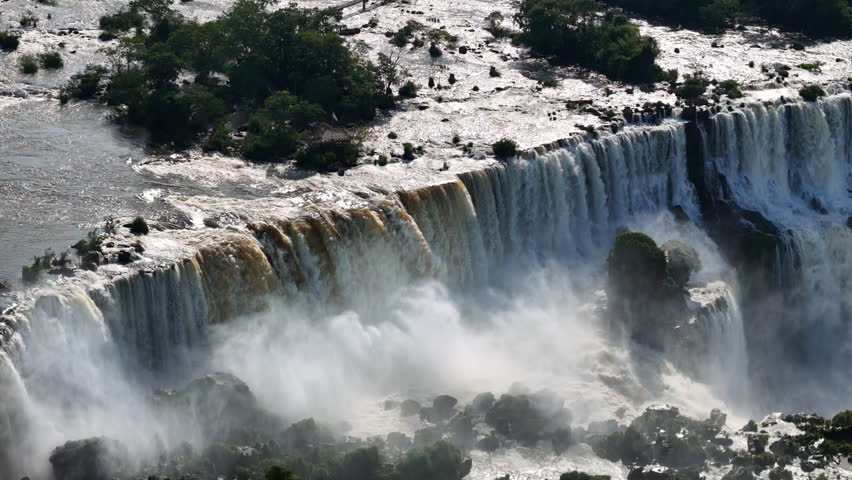 The scene follows Iguazu Falls in Brazil. Streams of water cascade into the canyon. Thick mist swirls above creating a breathtaking moving view of the waterfalls