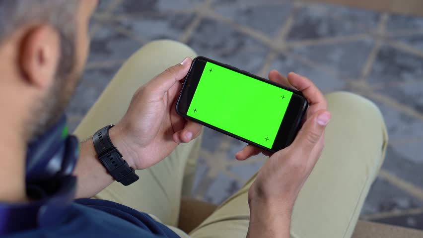 Top view of a man holding smartphone horizontally while lying on couch – green screen footage for video content