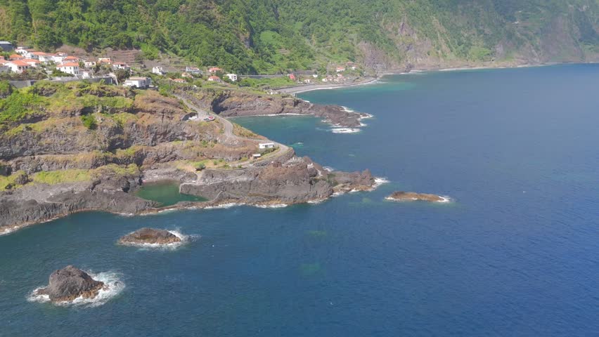 Aerial view of a coastal village perched on rugged cliffs with natural rock pools, turquoise waters, and ocean waves, capturing the harmony of traditional living and dramatic Atlantic scenery.