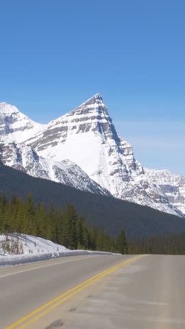 POV: Spectacular view of snowy peaks of the Canadian Rockies during a road trip along Icefields Parkway. Driving along an empty country road leading across Jasper National Park on a sunny winter day.
